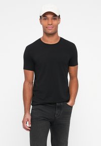 Camiseta negra de manga corta con escote redondo, combinada con jeans gris oscuro. Una gorra de color claro con el logo "BOSS" descansa sobre la cabeza.