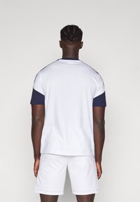 Korte mouwen t-shirt in het wit met marineblauwe accenten op de mouwen en kraag; gecombineerd met witte shorts. Katoenen materiaal, eenvoudig ontwerp.