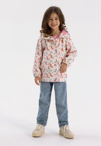Giacca impermiabile rosa chiaro con motivi di unicorni e arcobaleni, dotata di cappuccio, polsini elasticizzati e tasche, abbinata a jeans blu e sneaker.