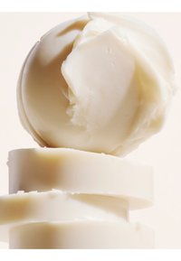 Plusieurs pains de savon ronds blancs empilés avec un pain partiellement utilisé sur le dessus, sur un fond clair.