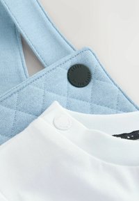 Modra prešita tkaninska brisača z črnim gumbom z oznako "TED BAKER" in bela majica s kratkimi rokavi z zapenjalnim gumbom v mehkobi.