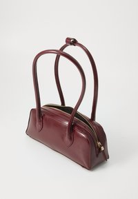 Sac à main en cuir bourgogne avec deux longues poignées, une fermeture éclair en haut, une forme arrondie et une texture lisse et brillante. Accent en métal doré.