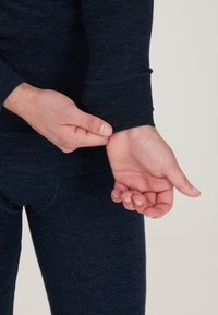 Marinblå termisk långärmad skjorta med en figursydd design, som har en ribbad manschett. Personens hand justerar ärmen och visar upp texturen.