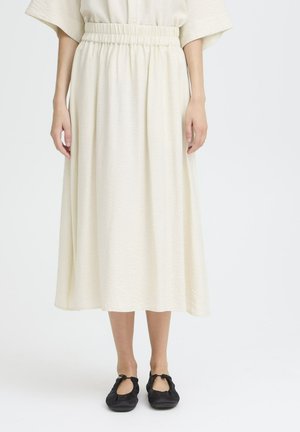 Kremowa midi spódnica z fakturowanej tkaniny, z elastycznym paskiem w talii i zwiewną sylwetką, w połączeniu z czarnymi butami typu slip-on.