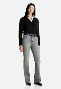 Un cardigan noir à boutons sur une chemise blanche, associé à un jean évasé gris délavé et des ballerines noires. Design simple avec une silhouette ajustée.