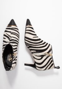 Zebra-gestreepte enkelboots met een vachtachtige textuur, spitse neus, zwarte leren accenten en een zijritsdetail in gouden hardware.