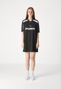 Vestido desportivo preto com mangas curtas, apresentando um logo da Puma branco, ombros cinzentos em contraste e um corte relaxado. Projetado para uso atlético.