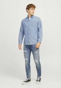 Világoskék farmering gombos dizájnnal és mellzsebbel, összeállítva kopott kék farmerral és fekete magasszárú sportcipőkkel.