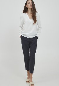 Witte blouse met lange mouwen en v-hals, gecombineerd met marineblauwe tapered broek. De outfit heeft een gladde textuur en een minimalistisch ontwerp.