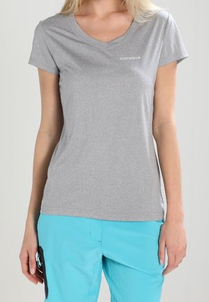 Kobieta nosząca dopasowany szary t-shirt z dekoltem w serek i małym logo oraz jasnoniebieskie spodnie z czarnym detalem kieszeni po boku.