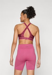 Roze sportski grudnjak s teksturiranim uzorkom i križno leđa, uparen s visokim roze šortsem koji ima rebraste detalje.