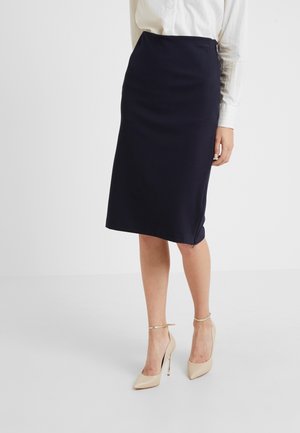 Femme portant une jupe crayon bleu marine longueur genou avec un chemisier blanc à manches longues et des chaussures à talons hauts beiges avec bride à la cheville.