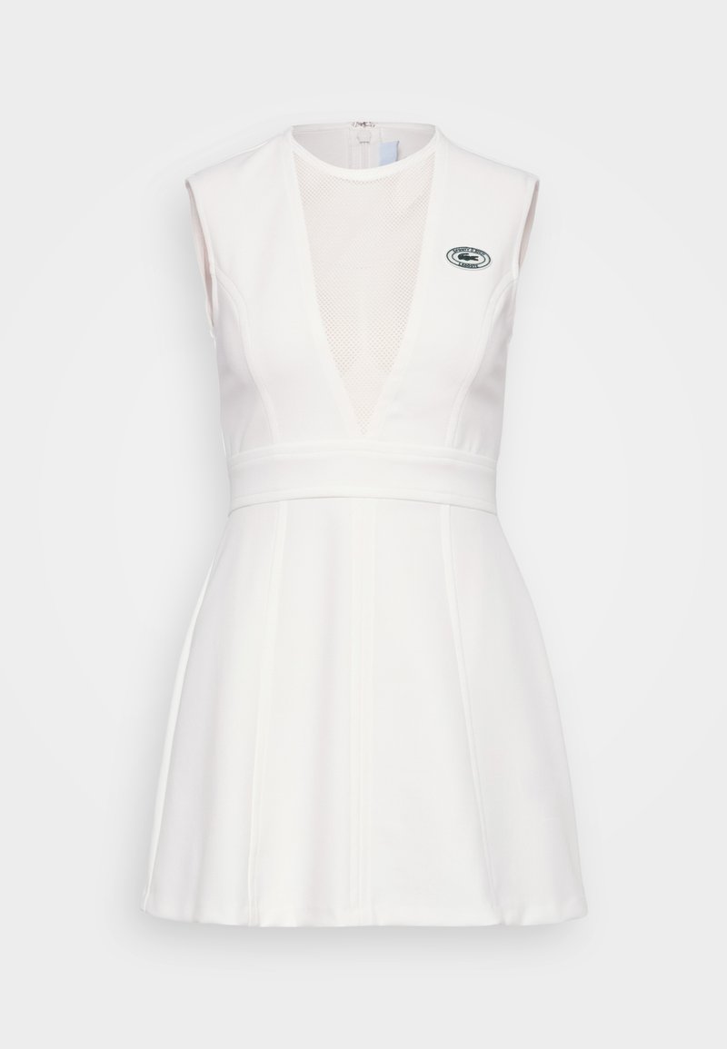 Biała sukienka bez rękawów z głębokim dekoltem w kształcie V i panelami z siateczki. Posiada dopasowaną talię i rozkloszowany krój. Zawiera akcent z logo z boku.
