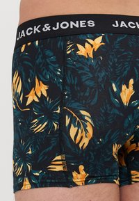 Schwarze Boxershorts mit einem tropischen Blumenmuster in Grün und Gelb, ausgestattet mit einem schwarzen elastischen Bund mit dem Logo "JACK & JONES".