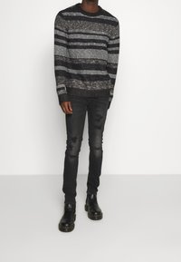 Randig stickad tröja i grå, svart och vit nyanser, kombinerad med svarta slitna jeans och svarta läderstövlar med kraftig sula.