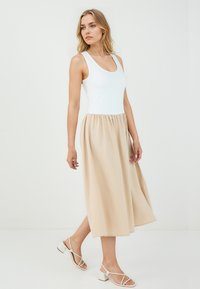Haut sans manches blanc avec un col rond, associé à une jupe midi fluide beige et des talons blancs à brides. Tissu doux et léger.