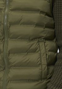 Maslinasto zeleni prsluk s punjenjem s horizontalnim šavovima, prednji zatvarač i bočne džepove. Glatka tekstura i lagan dizajn.