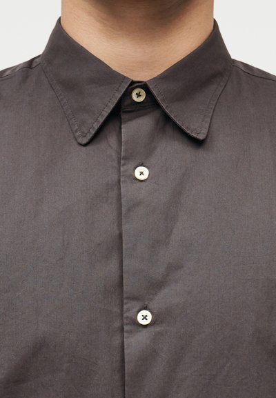 Κοντινό πλάνο ενός ατόμου που φοράει πουκ άμισο σκουρόγκρι με γιακά μυτερό και τρία λευκά κουμπιά δεμένα.