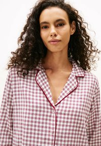 Biała bawełniana koszula do piżamy z czerwono-granatowym wzorem w kratę. Posiada kołnierz z wycięciem oraz kontrastujące czerwone lamówki wzdłuż krawędzi.