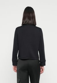 Sweatshirt noir court avec des manches longues, des poignets côtelés et une texture lisse. Présente un design simple sans embellissements visibles.