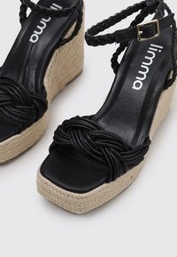 Schwarze gewebte Plateausandalen mit einem geflochtenen Oberdesign, einer strukturierten Jutewedge und einem glatten Lederfu ßbett. Mit Schnallenverschluss.