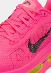 Ροζ αθλητικό παπούτσι με υφασμάτινη πλέξη στην επάνω πλευρά, μαύρο λογότυπο Nike και φωτεινής απόχρωσης σόλα. Διαθέτει κορδόνια και έντονη λεπτομέρεια απορρόφησης κραδασμών.