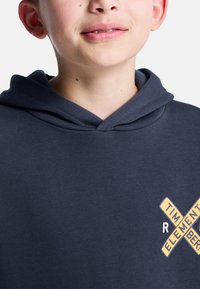 Felpa con cappuccio blu navy con tessuto strutturato. Presenta una grande stampa grafica con accenti gialli e un design del cappuccio a doppio strato.