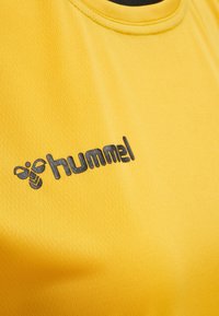 Gul sportströja i texturerad tyg med en svart "hummel"-logotyp. Designen inkluderar en rund halsringning och korta ärmar.