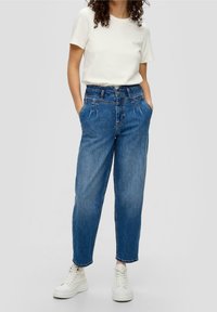 Light blue high-waisted jeans with a relaxed fit, featuring front pockets and pleated details, paired with a simple white t-shirt and white sneakers.