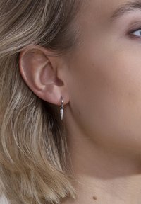Sidabrinė auskarų kilpa su smailiu pakabuku, turinti poliruotą paviršių. Dizainas yra minimalistas, su elegantiška ir modernaus stiliaus forma.