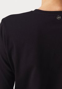 Svart crew neck-top med en slät textur, med en liten metallaccents på baksidan nära halsringningen och en klassisk passform.