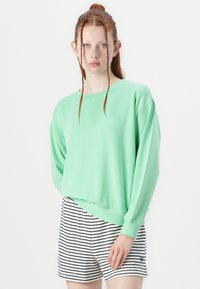 Felpa verde menta con maniche lunghe, polsini a costine, vestibilità rilassata, abbinata a pantaloni corti bianchi e blu a righe con un piccolo dettagliologo.