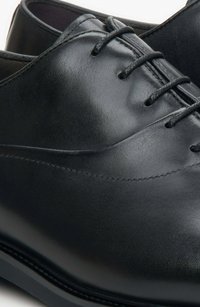 Czarne skórzane buty wizytowe o gładkiej fakturze, z detalami w postaci sznurowania i lekko zaokrąglonym noskiem. Posiadają niskoprofilową podeszwę i minimalne przeszycia.