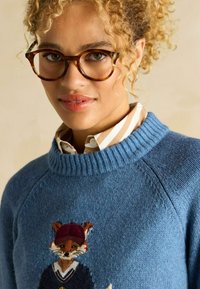 Pulover tricotat albastru cu un design cu vulpe, care poartă o pălărie și un pulover vișiniu. Guler cu dungi și țesătură texturată cu accente de albastru deschis.