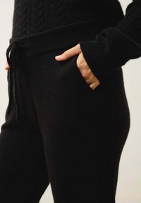 Svarta stickade joggers med elastisk midja och dragsko. Har ribbade manchetter och sidofickor, med en mjuk och texturerad yta.