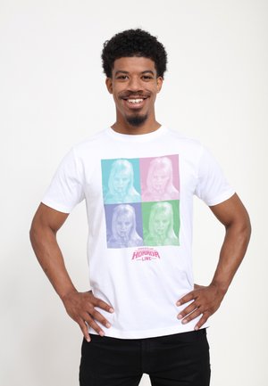 Hvid bomulds T-shirt med et popkunst-inspireret grafisk motiv af et ansigt i fire farver: lyserød, blå, grøn og lilla. Den inkluderer teksten "HORROR LINE".