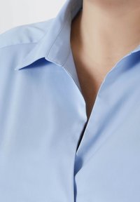 Blouse bleu clair avec un col classique et une texture lisse. Présente un devant à boutons et une légère brillance. Détails de design épurés et simples.