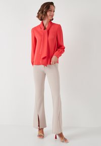 Kirkas oranž blouse, millel on lipsu detail, pikad varrukad, koos heledate beežide flare-pükstega, millel on lõhed ääres ja värvikad kontsad.
