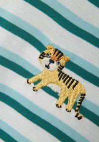 Un tessuto a strisce in azzurro chiaro e bianco presenta un tigre gialla ricamata con strisce nere, che mostra cuciture e texture dettagliate.