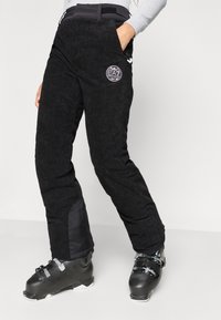 Μαύρο παντελόνι σκι από κοτλέ με εφαρμοστή σχεδίαση, διαθέτει τσέπες με φερμουάρ και λογότυπο στη μέση. Ενισχυμένο μαύρο ύφασμα στις γάμπες.