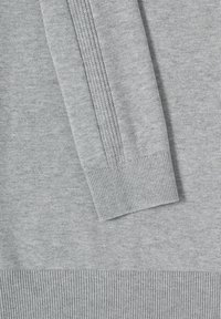 Gros plan sur la manche d'un pull gris en tricot avec un poignet côtelé et un détail de tricot vertical le long du bras.