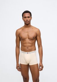 Μπεζ βαμβακερές μποξέρ με φαρδύ ελαστικό ζωνάκι που φέρει το λογότυπο "TOMMY HILFIGER" σε σκούρα γράμματα και μια μικρή χρωματιστή λεπτομέρεια.
