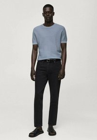 Tricou tricotat texturat, de culoare albastru deschis, cu mânecă scurtă, blugi negri și sandale negre. Blugi cu croi drept și un centură simplă. Fără modele sau logo-uri vizibile.