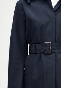 Ναυτικό μπλε παλτό τύπου trench με μακριά μανίκια και φαρδιά ζώνη στην ίδια απόχρωση με ορθογώνια μαύρη αγκράφα, που εμφανίζει μπροστινή τσέπη και γιακά.