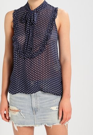 Blusa sin mangas azul marino con estampado de estrellas blancas y volantes, combinada con una mini falda vaquera desgastada en azul claro.