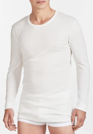 Maglietta termica bianca a maniche lunghe realizzata in tessuto leggero e liscio, con un colletto a girocollo e un design aderente, indossata con pantaloni intimi bianchi.