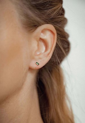 Grüner rechteckiger Ohrstecker aus Metall, mit glatter Oberfläche und minimalistischem Design, abgebildet vor einer Nahaufnahme eines Ohres.