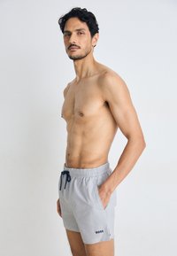 Calções de banho às riscas em azul-marinho e branco com cintura elástica e cordão, apresentando bolsos laterais e um pequeno detalhe de logótipo.