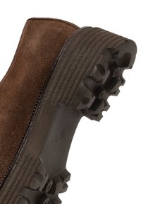 Brauner Wildleder-Stiefelette mit strukturiertem Gummisohlenprofil, das ein Zickzackmuster und horizontale Rillen für besseren Halt aufweist.