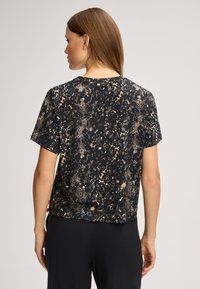 Svart kortärmad topp med ormmönster i nyanser av beige och brunt. Tillverkad av ett lätt, texturerat tyg.